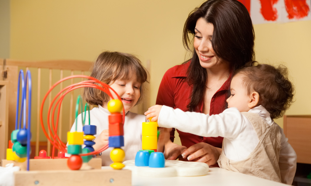 Two kids playing with blocks with a woman wearing a red shirt