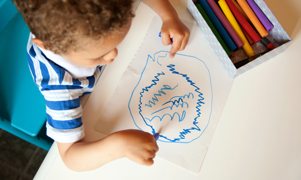 A kid drawing curve lines using a blue crayon